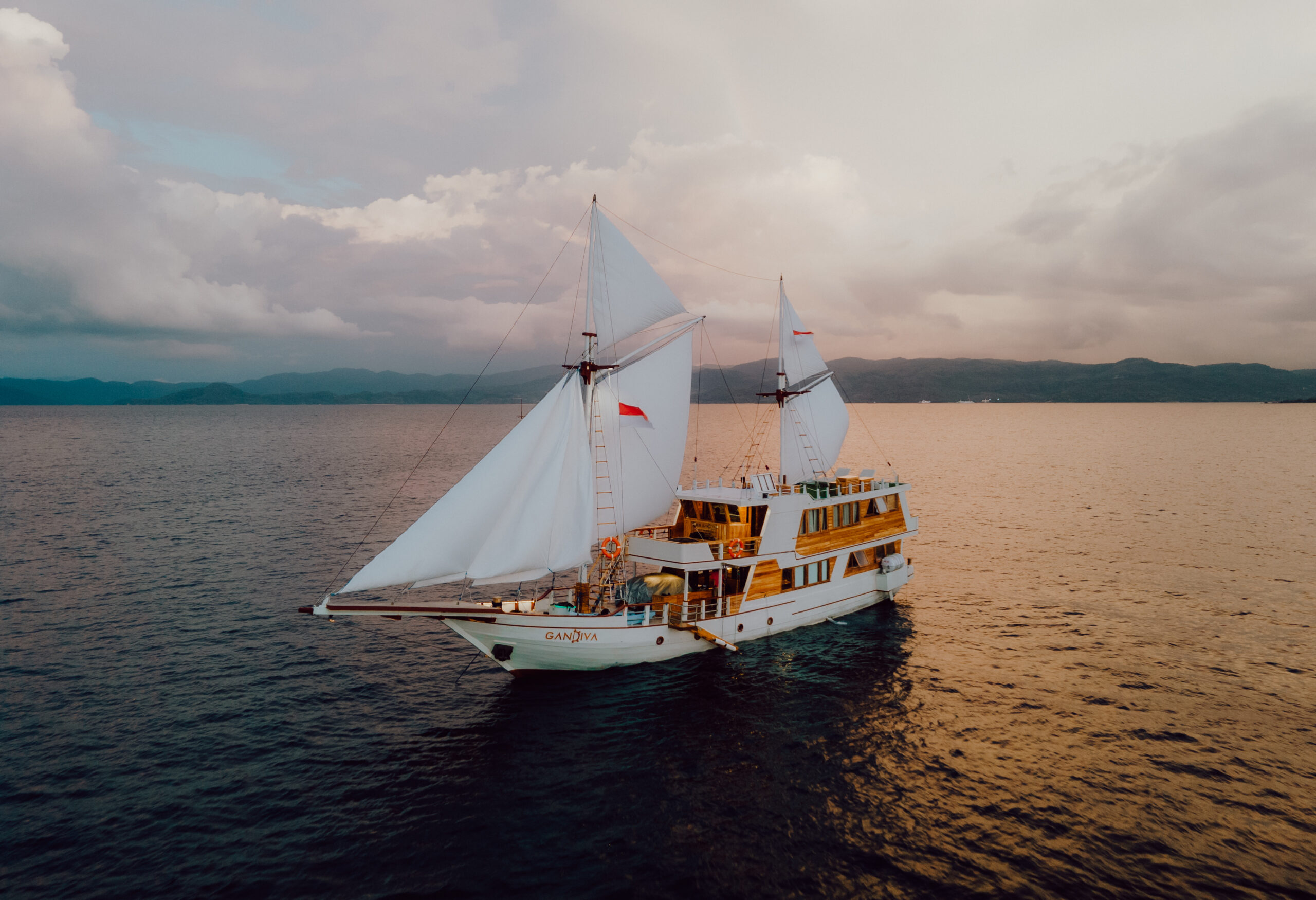 Gandiva Phinisi sailboat sailing in Komodo National Park during sunset.