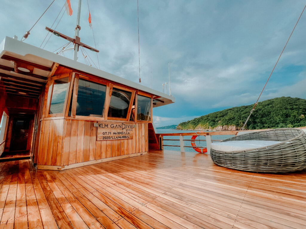 Deck of the Gandiva Phinisi boat in Komodo National Park, showcasing wooden flooring and scenic surroundings.