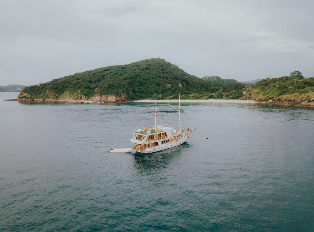 Gandiva Phinisi boat anchored in calm waters near a green island in Komodo National Park.