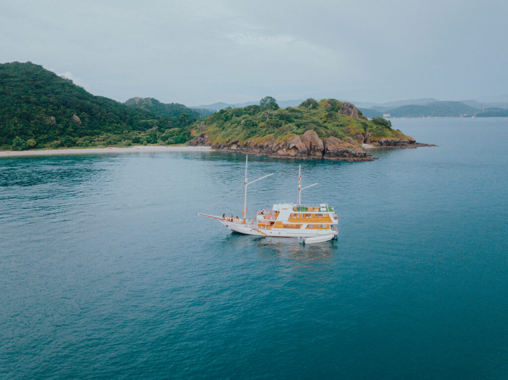 Gandiva phinisi boat sailing in Komodo National Park with lush islands in the background.