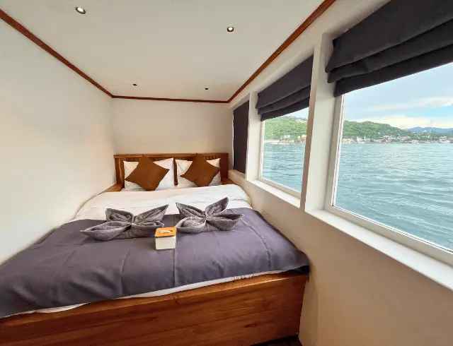 Interior of a deluxe cabin on the Lanakila, featuring a bed and large windows with a water view.